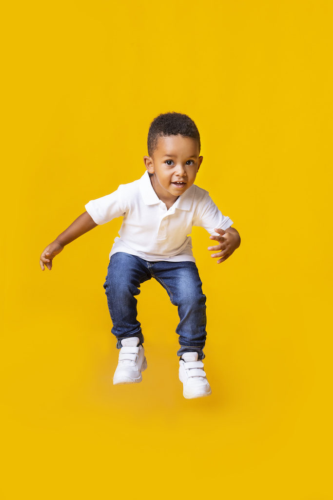 Adorable afro baby boy jumping over yellow studio background with copy space